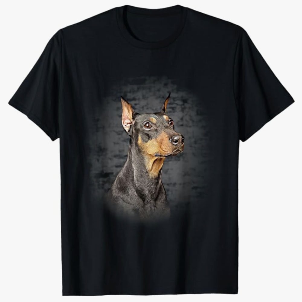 Black T-shirt featuring a realistic portrait of a Doberman Pinscher on a dark textured background, highlighting the breed’s strength, intelligence, and elegance.