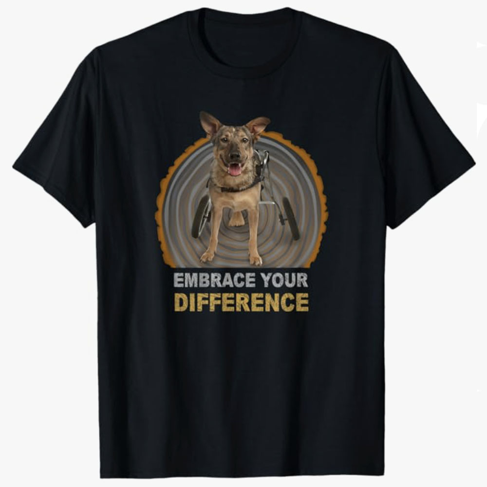 Black T-shirt featuring a happy dog using a wheelchair with the text Embrace Your Difference, promoting inclusivity, resilience, and the beauty of individuality through an inspiring design.