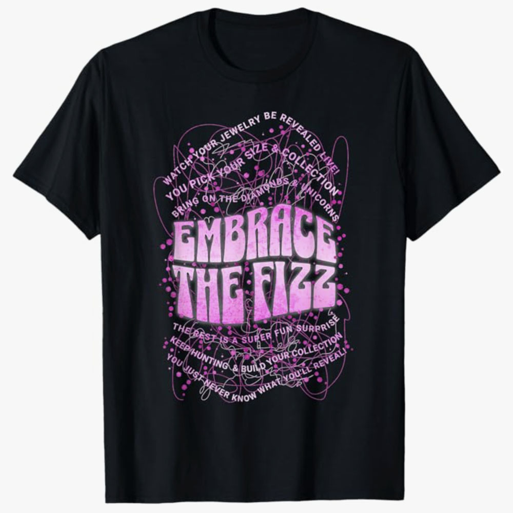 A black T-shirt features bold pink lettering reading Embrace the Fizz surrounded by energetic scribble lines and playful text about surprise jewelry reveals. The design conveys excitement, mystery, and the joy of embracing unexpected sparkle.