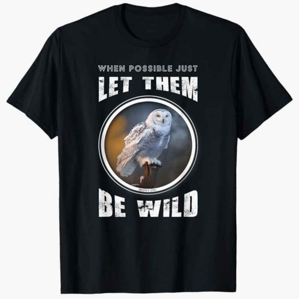 A black T-shirt features a snowy owl inside a circular frame with the words “When possible just let them be wild.” The design promotes respect for wildlife and the importance of allowing animals to live free.