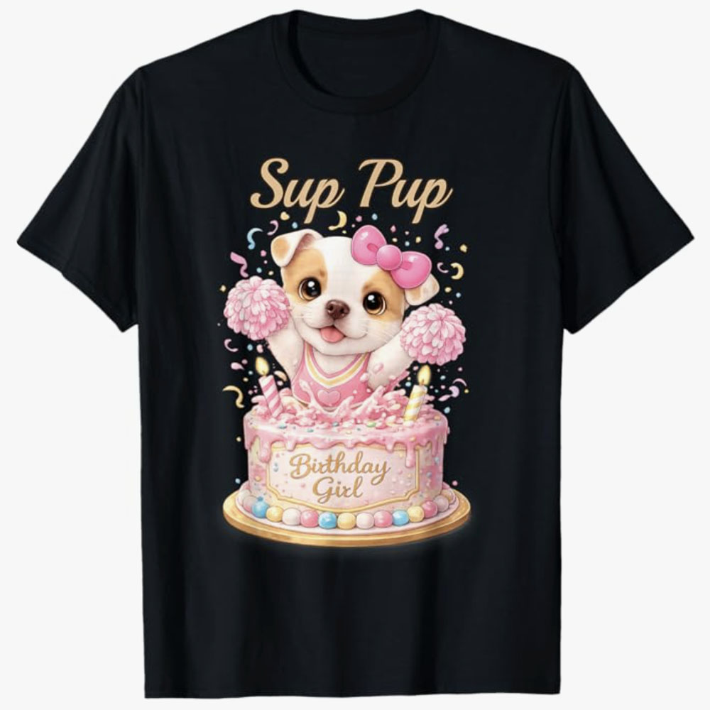 A black T-shirt shows a cute cartoon puppy with a pink bow popping out of a birthday cake with the phrase Sup Pup, creating a playful design for celebrating a birthday girl.