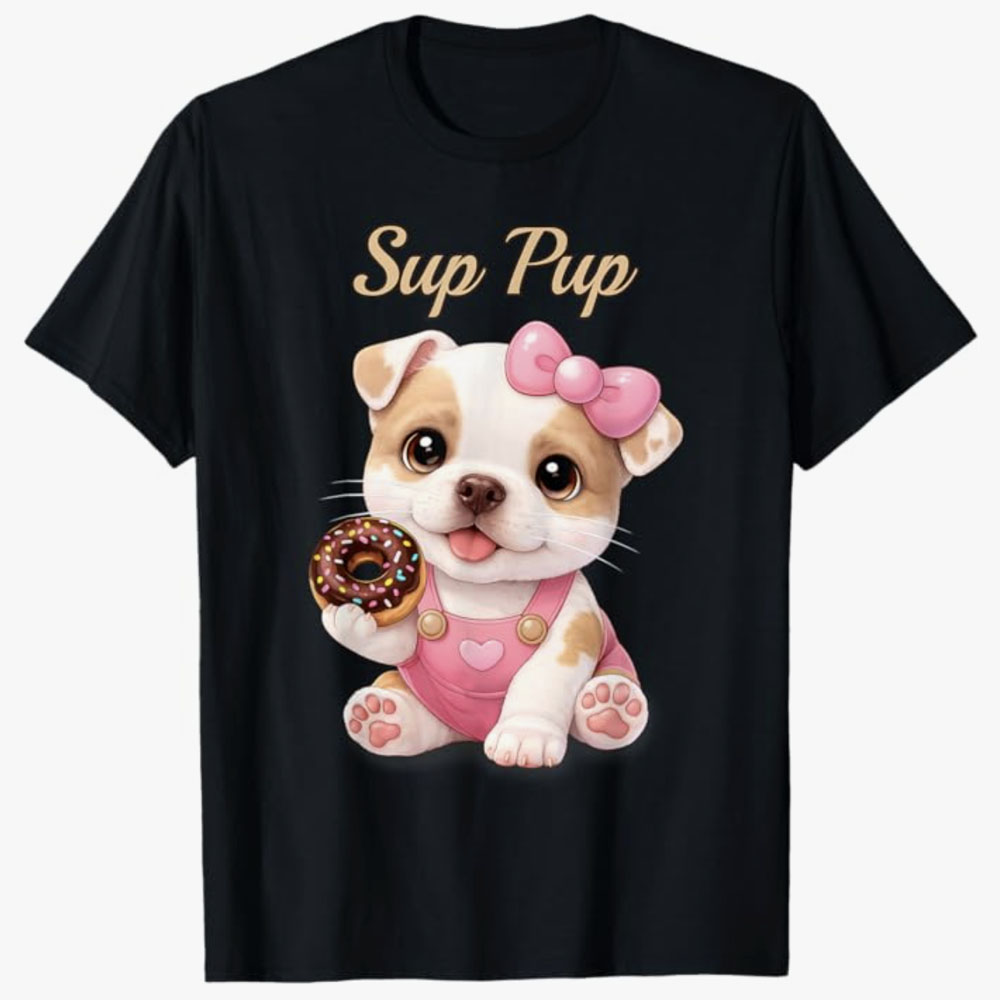 A black T-shirt shows a cute cartoon puppy with a pink bow holding a sprinkled donut under the phrase Sup Pup, creating a playful and sweet design for dog lovers.