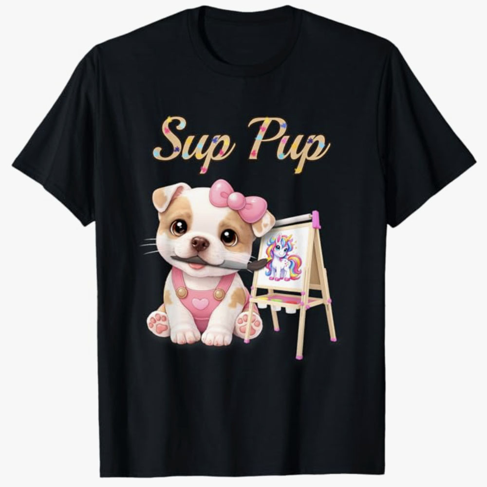 A black T-shirt shows a cute cartoon puppy with a pink bow painting a colorful unicorn beside the playful phrase Sup Pup, celebrating creativity and fun for dog lovers.