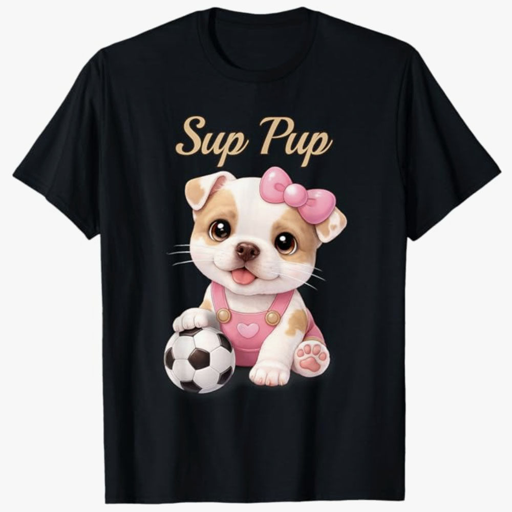 A black T-shirt shows a cute cartoon puppy with a pink bow sitting beside a soccer ball under the phrase Sup Pup, combining playful dog charm with a fun sports theme.